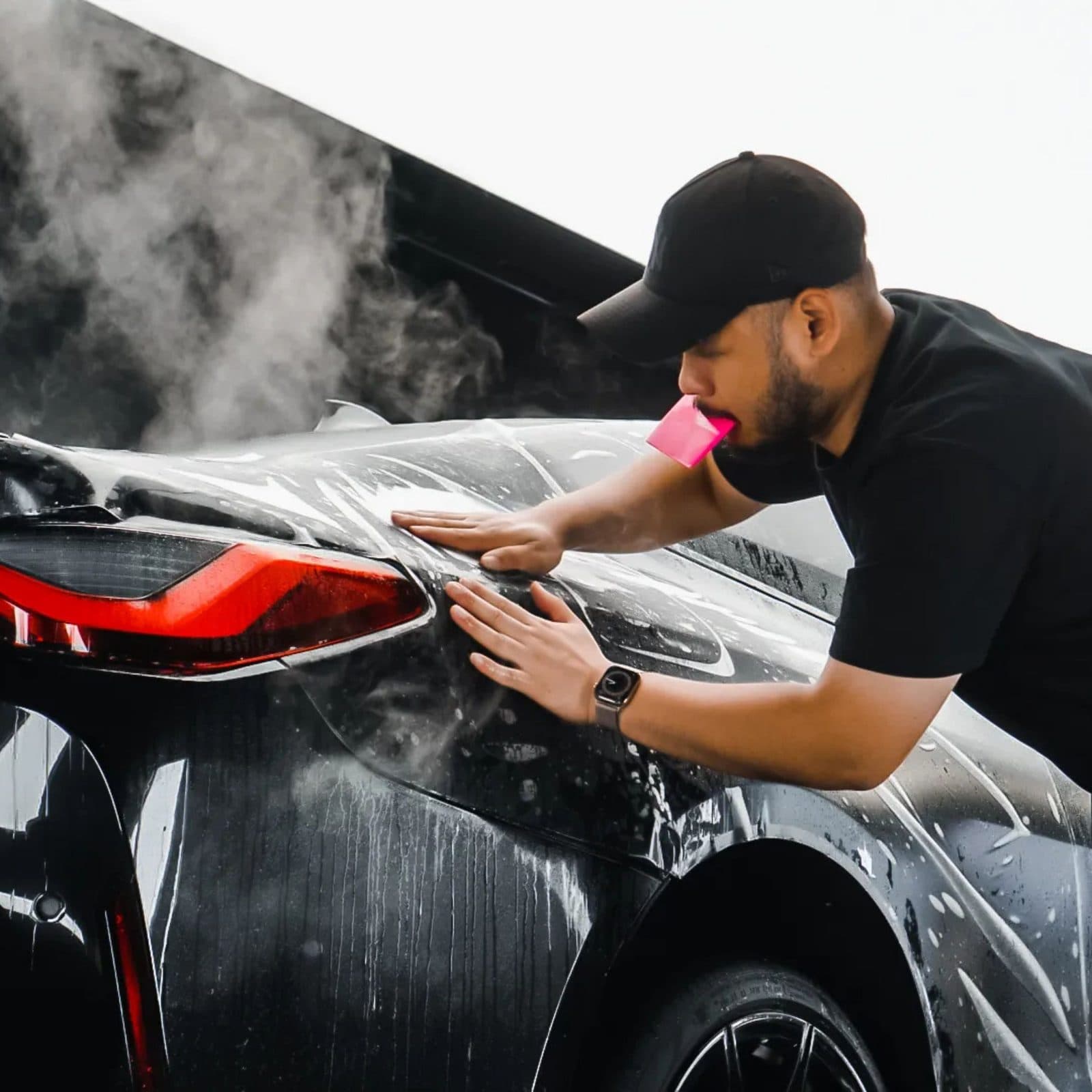 Clear paint protection film being squeegeed onto the rear quarter of a black sports car